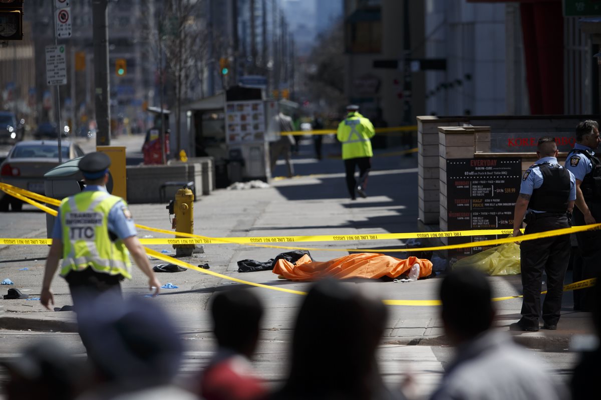 Policías cubren el cuerpo de una de las víctimas del atropellamiento en Toronto, Canadá. (Foto Prensa Libre: AFP)
