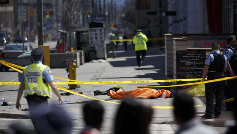 Policías cubren el cuerpo de una de las víctimas del atropellamiento en Toronto, Canadá. (Foto Prensa Libre: AFP)