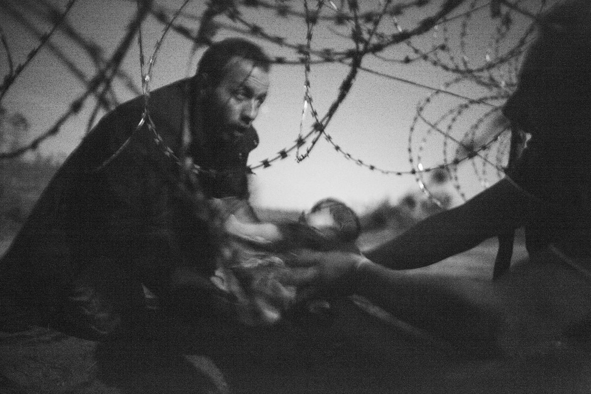Foto ganadora del World Press Photo; el fotógrafo australiano Warren Richardson muestra un hombre pasando a un bebé a través de la valla de alambre de espino en Roeszke, frontera entre Serbia y Hungría. (Foto Prensa Libre: EFE).