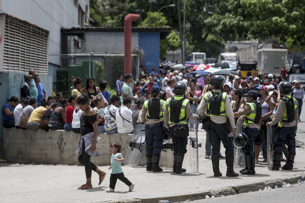 Policías venezolanos vigilar el orden en una fila de personas que busca ingresar a un supermercado. (Foto Prensa Libre: EFE).