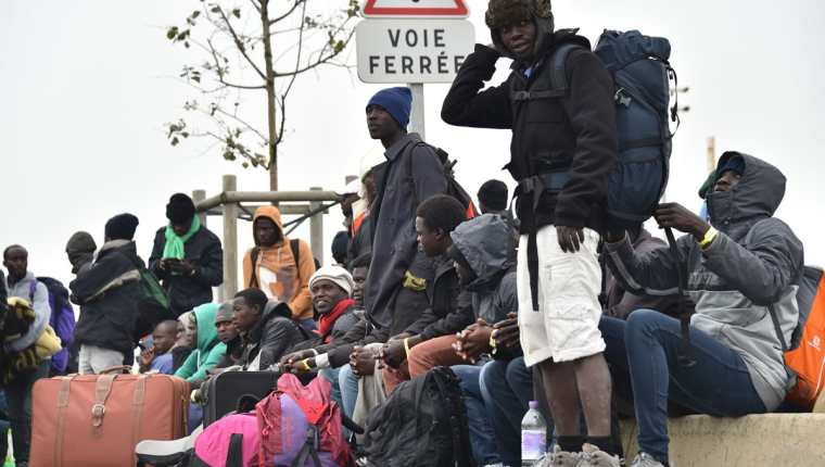 Migrantes en Calais esperan el transporte que los llevará a su nuevo refugio. (Foto Prensa Libre: AFP).