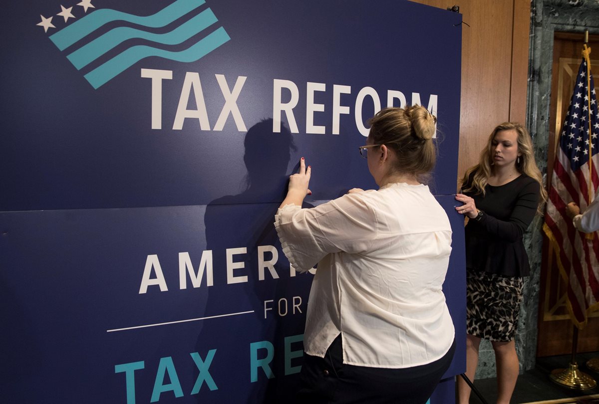 Empleados colocan un cartel en el que se lee "Tax Reform" (Reforma fiscal) durante un acto para promover el plan republicano de reforma fiscal, en el Capitolio. (Foto Prensa Libre: EFE)