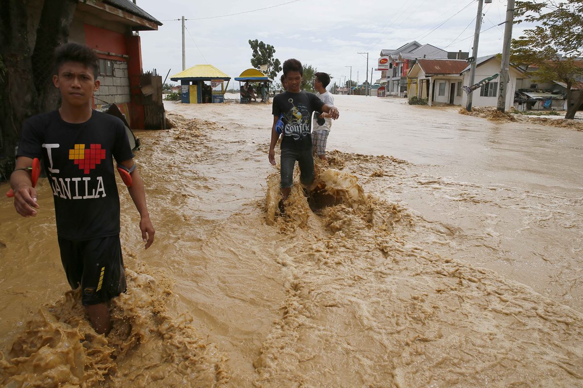 Jóvenes tratan de cruza una alle inundada en Filipinas. (foto Prensa Libre: AP).