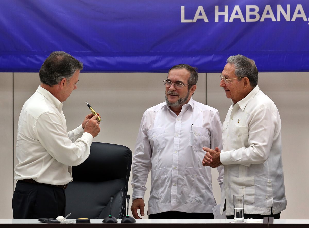 Juan Manuel Santos (izq.) presidente de Colombia, regala una pluma a Rodrigo Londoño (cent.) de las Farc, en presencia de Raúl Castro, presidente de Cuba. (Foto Prensa Libre: EFE).