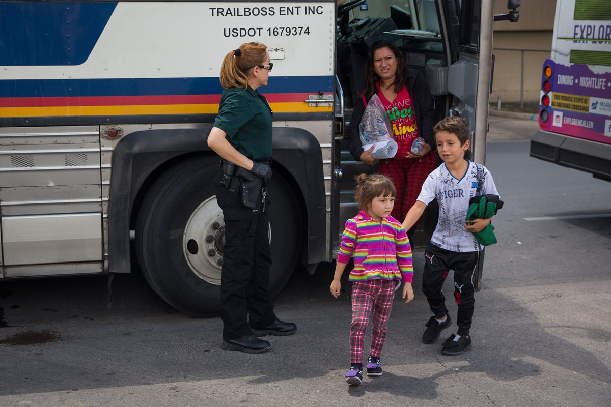Una agente de migración observa a una familia en McAllen, Texas, después de haber sido detenidos en la frontera. (Foto Prensa Libre: AFP)