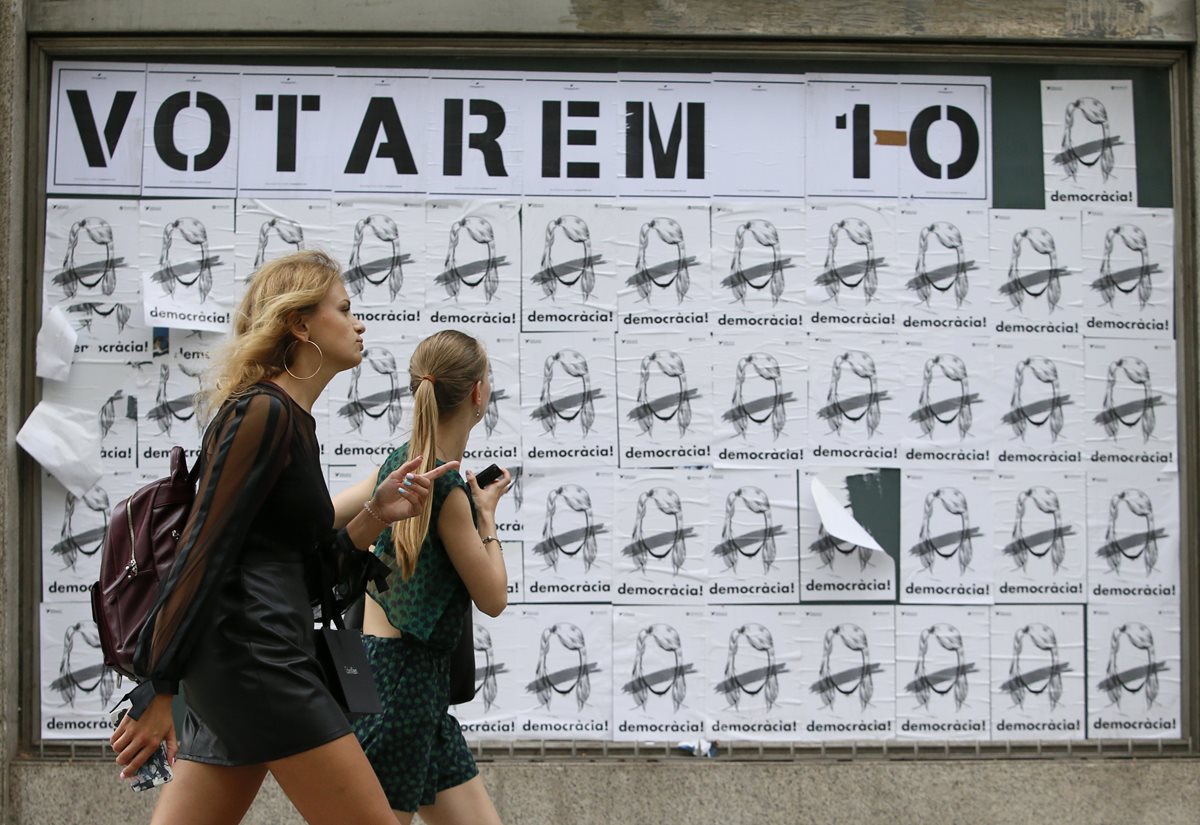Dos mujeres pasan frente a una propaganda que invita a los catalanes "Vamos a votar" en Barcelona. (AP).