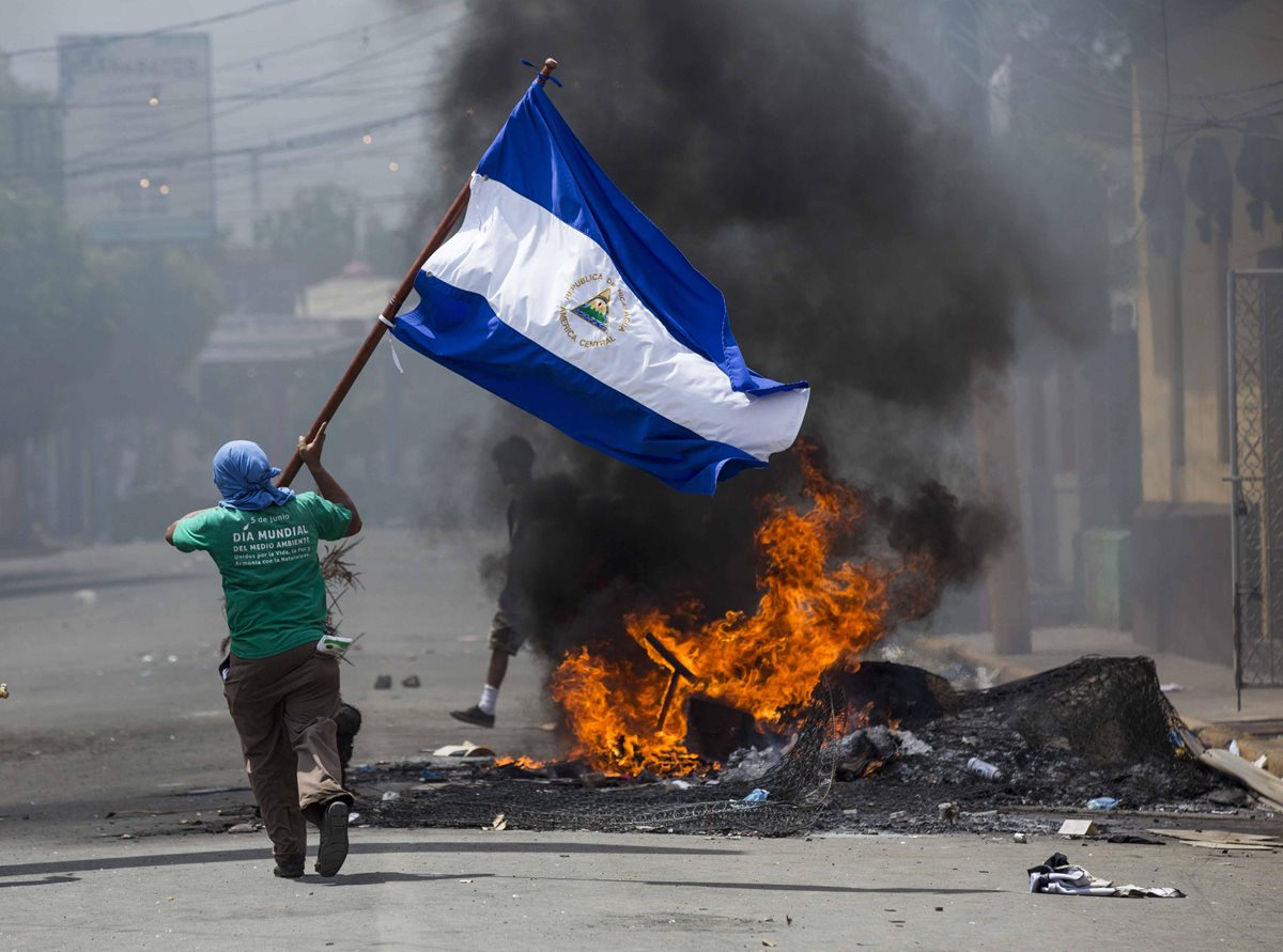 Un hombre corre con la bandera de Nicaragua entre los enfrentamientos entre policías y ciudadanos. (Foto Prensa Libre: EFE)
