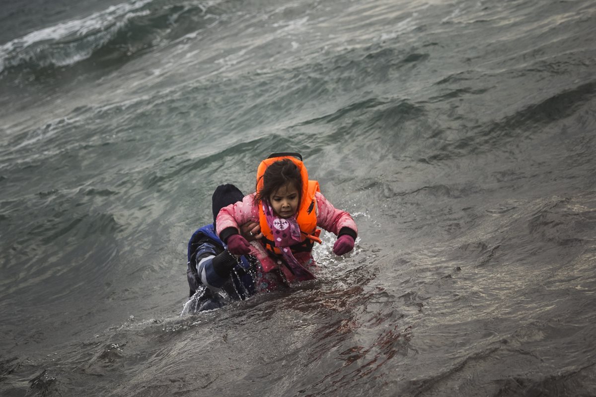 Un hombre trata de poner a salvo a una niña después de desembarcar en las costas del mar Egeo. (Foto Prensa Libre: AP).