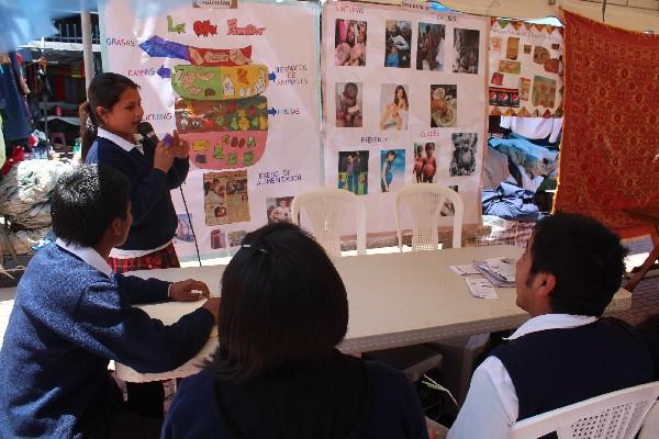 una estudiante les explica    hábitos de buena alimentación a    asistentes a la actividad.