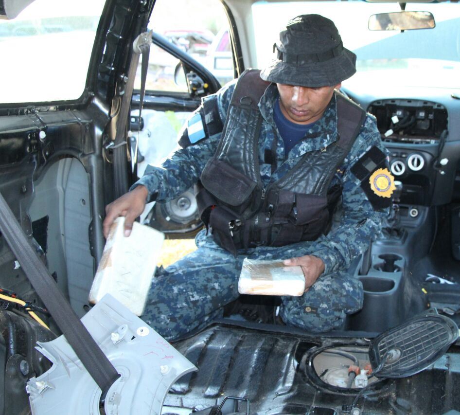 Un agente antinarcótico de la Policía Nacional Civil inspecciona uno de los vehículos localizados en el predio del Organismo Judicial de Cantel. (Foto Prensa Libre: PNC)