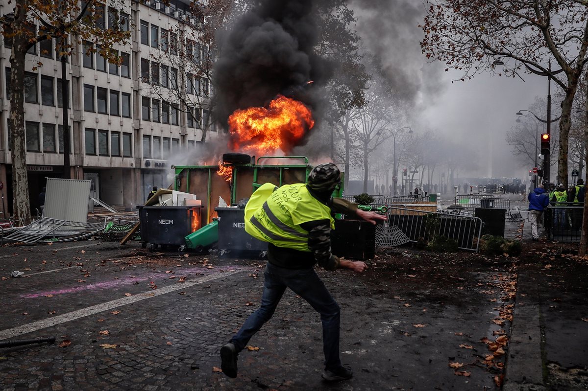 Un manifestante de los autodenominados "chalecos amarillos" se enfrentó a los agentes junto a una barricada en llamas durante los disturbios. (Foto Prensa Libre: EFE)