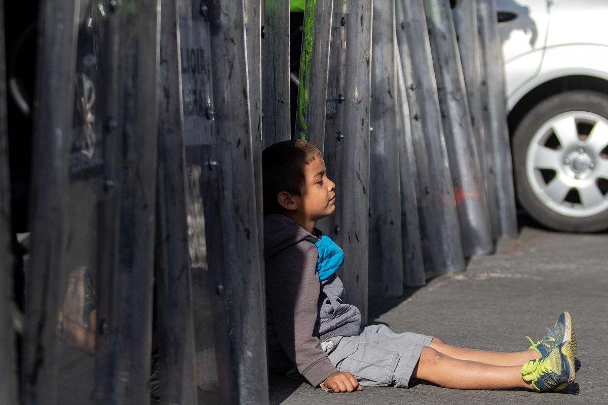 Un niño migrante centroamericano se sienta frente al cerco policial de antimotines que también México colocó. (Foto Prensa Libre: AFP)