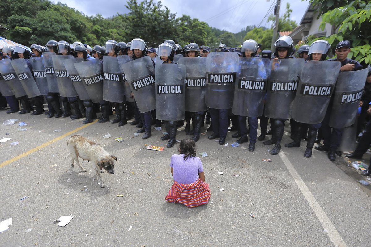 Una niña migrante hondureña se arrodilla frente un retén policial en la aduana de Agua Caliente, en Ocotepeque, Honduras. (Foto Prensa Libre: EFE)
