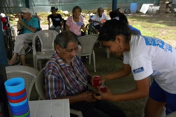 Una estudiante entrega un vaso con fresco a una persona de la tercera de edad que vive en el asilo Dulce Refugio, en San Gabriel. (Foto Prensa Libre: Omar Méndez)