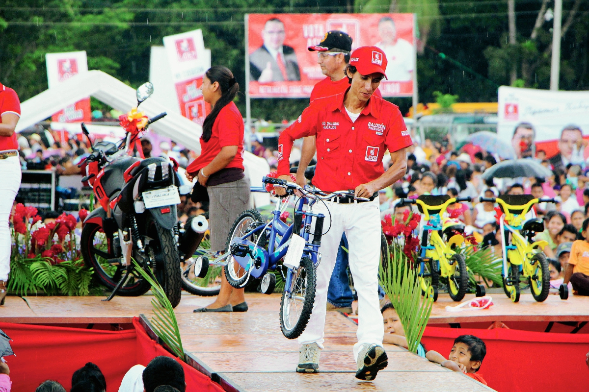 Un animador del partido Líder lleva una bicicleta que regalaron en el mitin en Caballo Blanco, Retalhuleu. (Foto Prensa Libre: Rolando Miranda)