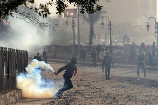 Un egipcio se dispone a devolver un cartucho de gas lacrimógeno lanzado por la Policía. (Foto Prensa Libre: AFP)