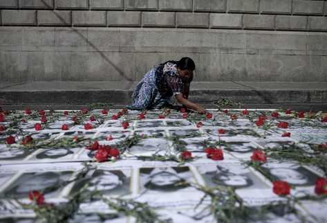 Una indígena coloca unas rosas sobre imágenes de víctimas del  conflicto armado. (Foto Prensa Libre: EFE)