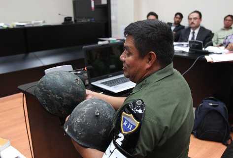 El Coronel Juan Chiroy muestra en la audiencia dos cascos con daños, los cuales supuestamente portaban  soldados el día de los disturbios en los que   murieron seis personas.