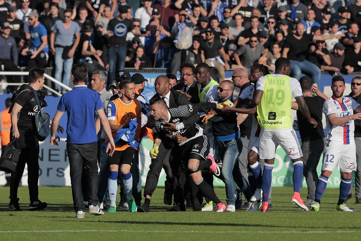 El portero del Lyon, Anthony Lopes es sostenido por un agente de seguridad, mientras los aficionados del Bastia intentan alcanzarlo. (Foto Prensa Libre: AFP)