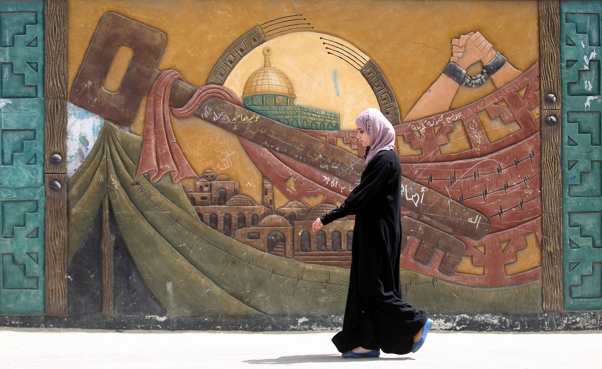 (Foto de referencia). Una palestina camina frente a un mural cerca de un campo de refugiados en Gaza. (Foto Prensa Libre: AFP).