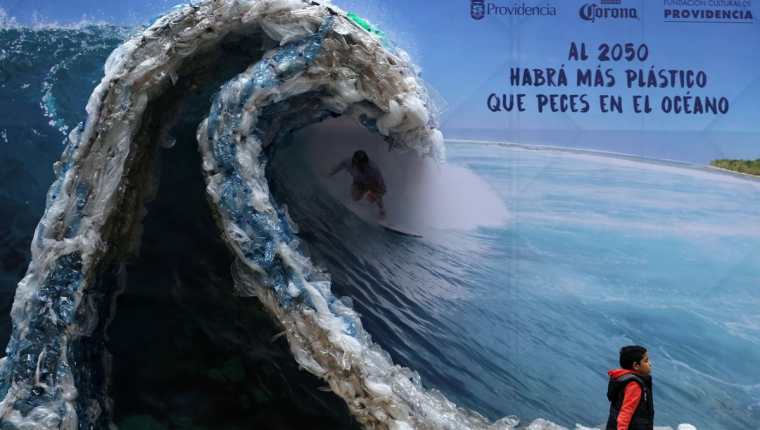 Una Manta publicitaria retrata a un hombre, surfeando una ola hecha de bolsas de plástico y botellas, para denunciar la contaminación de los océanos con motivo del Día Mundial del Medio Ambiente.(Foto prensa Libre:AFP)