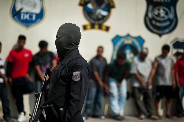 Un policía vigila a presuntos miembros de pandillas y colaboradores de éstos, San Salvador. (Foto Prensa Libre: AFP)