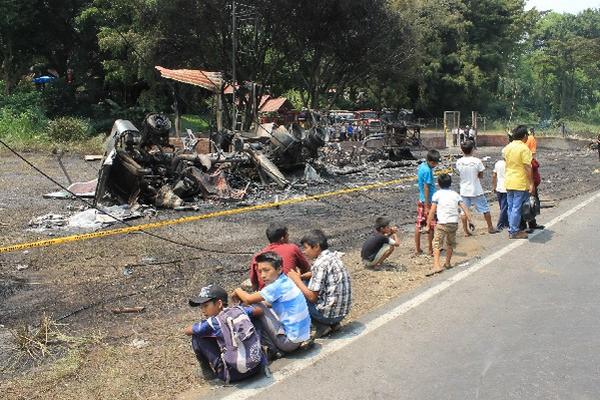 Niños permanecen junto a los restos del camión cisterna  incendiado, que quedó a la orilla de la carretera.