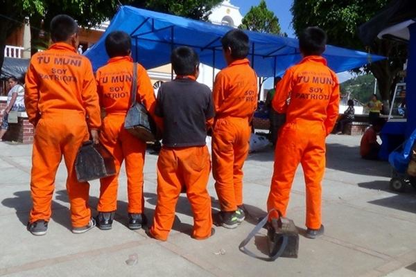 Un grupo  de niños limpiabotas muestra el overol naranja que les proporcionó la comuna de Cunén. (Foto Prensa Libre: Óscar Figueroa)