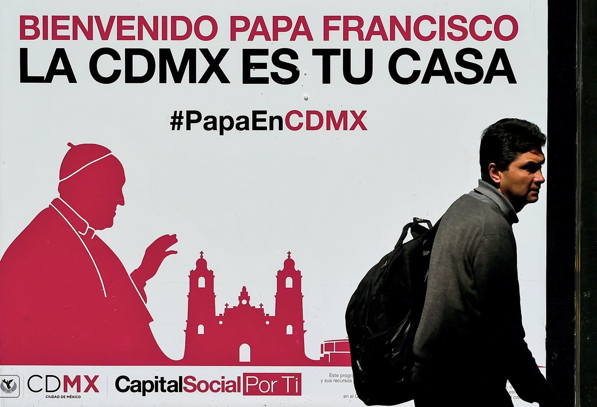Un peatón en Ciudad de México pasa frente a un rótulo de bienvenida al Papa. (Foto Prensa Libre: AFP).