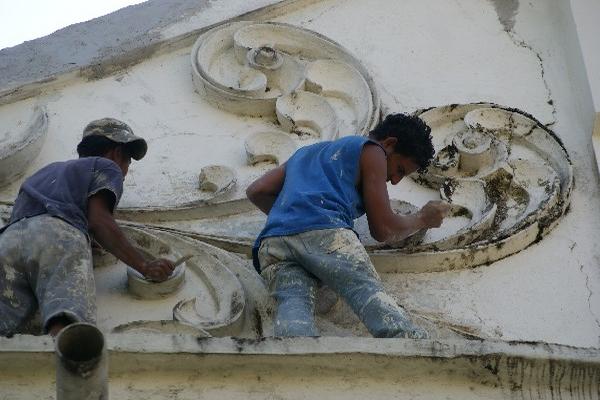 Dos empleados pintan la parte exterior de la iglesia católica de Retalhuleu.