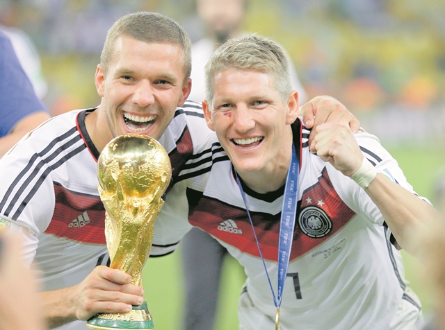 Lukas Podolski y Bastian Schweinsteiger junto al trofeo de la Copa del Mundo que ganaron en el Mundial de Brasil 2014. (Foto Prensa Libre: AP)