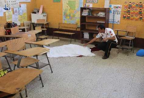 Un bombero Voluntario cubre el cuerpo de Juan Armando Coy Caal, de 13 años, que yace en el salón de tercero primaria, donde estudiaba.