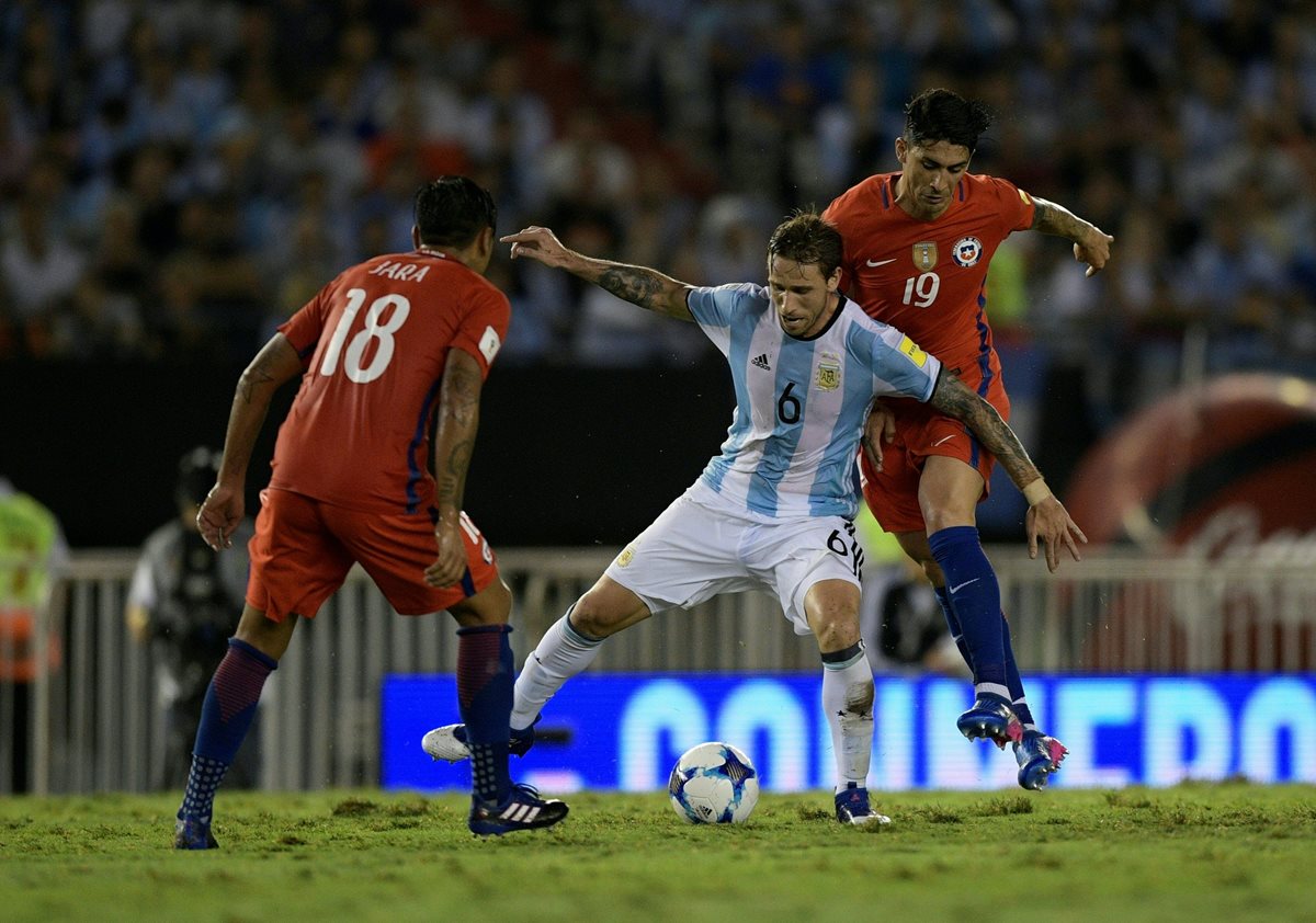 Lucas Biglia intenta cubrir la pelota ante la marca de dos jugadores chilenos.