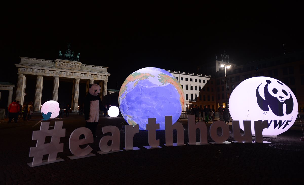 Un activista de WWF vestido como un oso panda se encuentra junto a un globo iluminado frente a la Puerta de Brandenburger en Berlín durante "La Hora del Planeta". (Foto Prensa Libre:AFP).