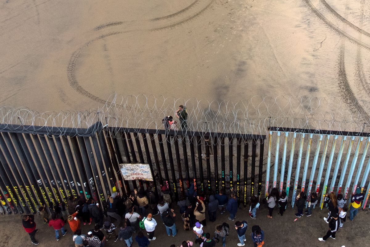 Migrantes observan hacia territorio estadounidense desde la frontera de Tijuana, México. (Foto Prensa Libre: AFP)