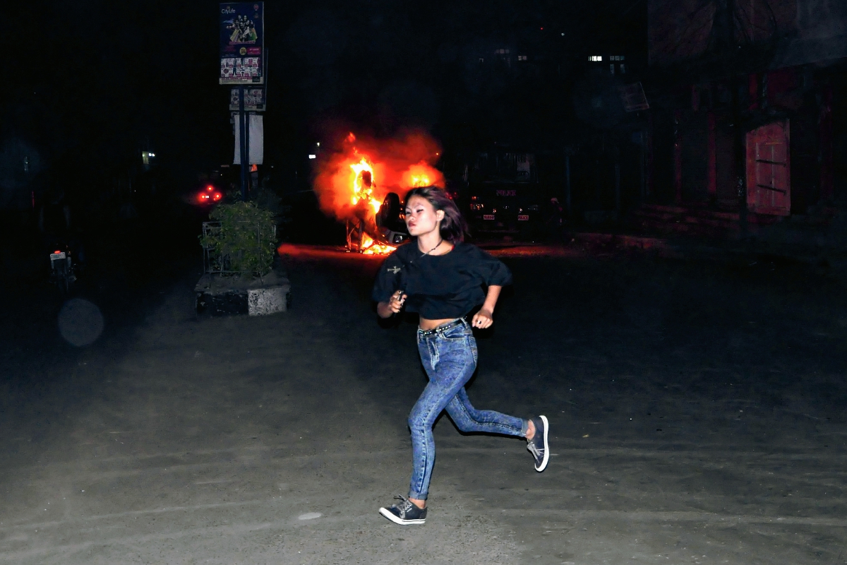 Una mujer no identificada corre frente a un carro en llamas producto de los disturbios ocurridos después del linchamiento de un supueto violador. (Foto Prensa Libre: AP).