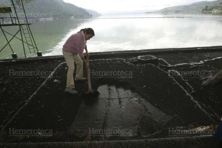 Una persona limpia de ceniza un chalet en la orilla del Lago de Amatitlán.