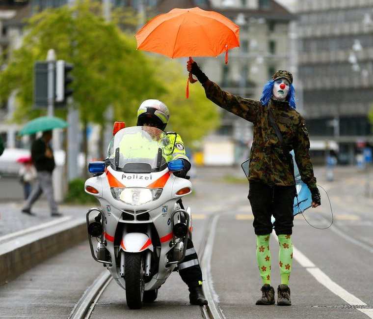 Un manifestante vestido de payaso cubre a un policía con su paraguas durante las protestas del 1 de Mayo en Zurich, Suiza. ARND WIEGMANN / REUTERS