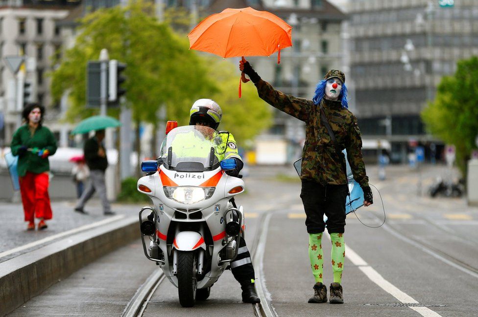 Un manifestante vestido de payaso cubre a un policía con su paraguas durante las protestas del 1 de Mayo en Zurich, Suiza. ARND WIEGMANN / REUTERS