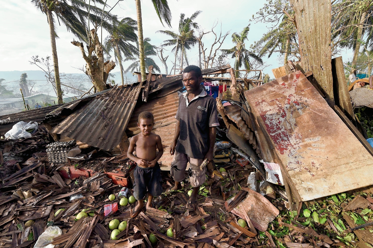 Un niño y su padre buscan rescatar algo de su casa en ruinas, tras el paso de Pam en Vanuetu. (Foto Prensa Libre: AFP).