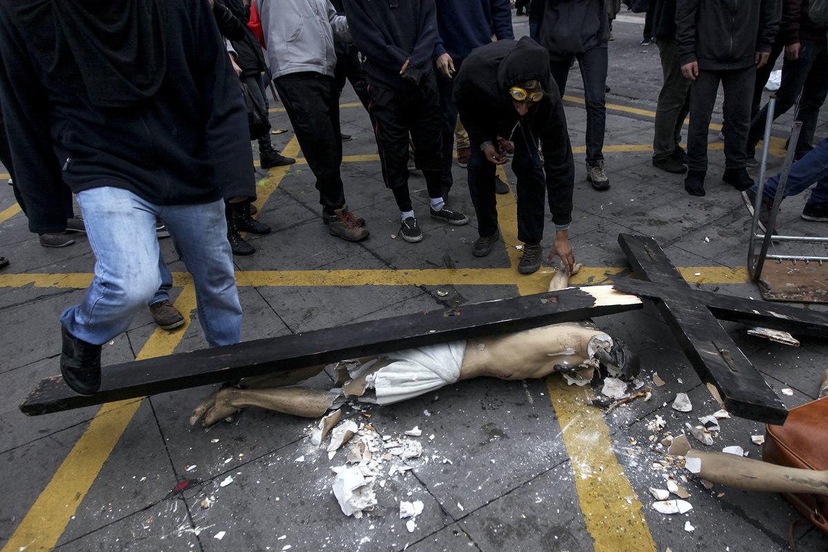 Un grupo de hombres enmascaradaos alrededor del Cristo que destruyeron luego de sacarlo de la iglesia. (Foto Prensa Libre: AP).