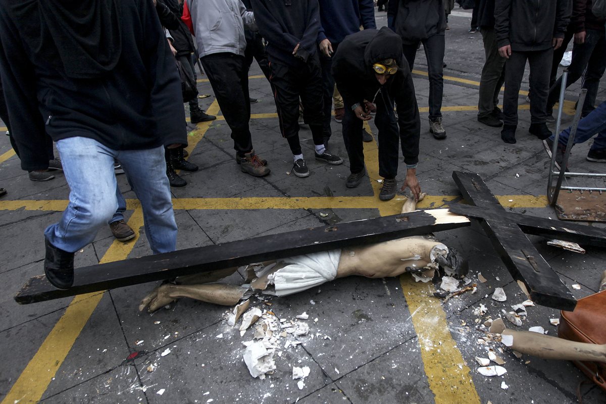 Un grupo de hombres enmascaradaos alrededor del Cristo que destruyeron luego de sacarlo de la iglesia. (Foto Prensa Libre: AP).