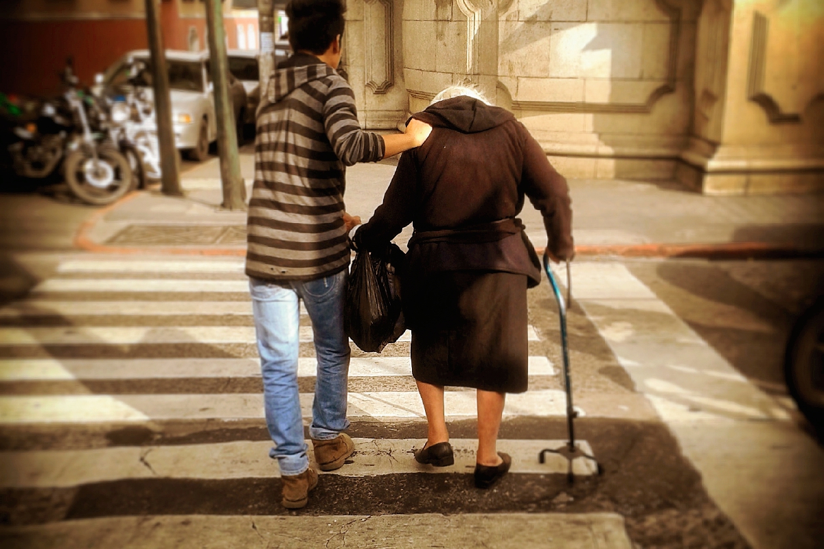 Un joven ayuda a un adulto mayor a cruzar la calle. (Foto Prensa Libre: Antonio Jiménez)