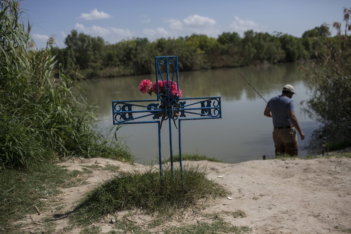 un hombre pesca en el río cerca de una cruz en memoria de un migrante que murió tratando de cruzar a EE.UU. a orillas del Río Grande en Nuevo Laredo. (AP).