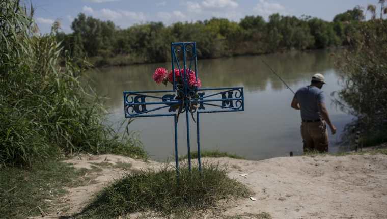 un hombre pesca en el río cerca de una cruz en memoria de un migrante que murió tratando de cruzar a EE.UU. a orillas del Río Grande en Nuevo Laredo. (AP).