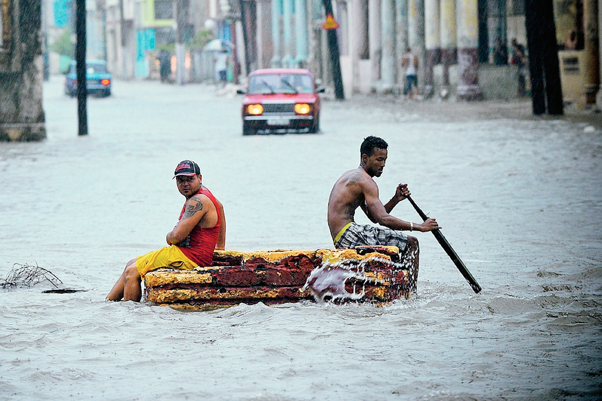 Dos hombres en una balsa improvisada cruzan una calle inundada  en La Habana,Cuba. (Foto Prensa Libre:AFP)