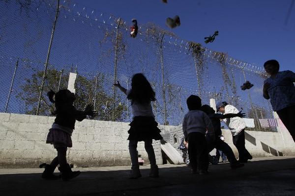 Un grupo de menores lanzan juguetes al aire, frente a una malla perimetral electrificada, en el COF.