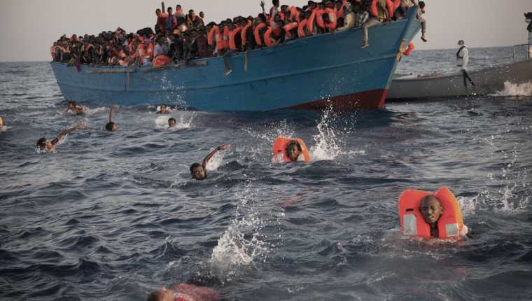 Migrantes desesperados se lanzan de bote a punto de zozobrar, en costa libia. (Foto Prensa Libre: AP)
