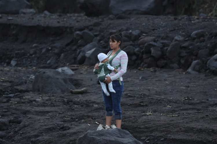 Una mujer espera con su hijo en brazos a pasar el río.