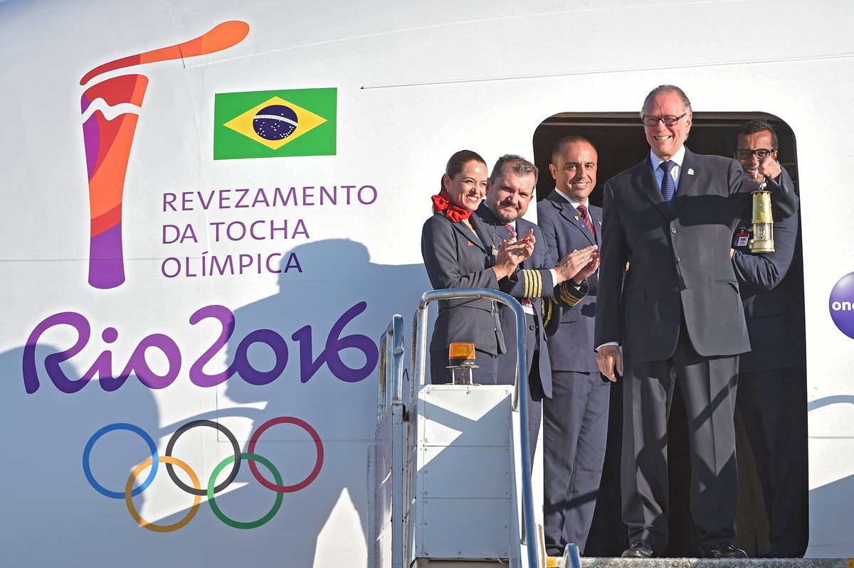 El presidente del Comité Olímpico Brasileño, Carlos Arthur Nusmann, muestra el fuego olímpico desde la puerta del avión, luego de aterrizar este martes en la capital brasileña. (Foto Prensa Libre: AFP)